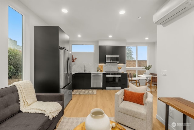 kitchen with backsplash, light hardwood / wood-style flooring, a wall unit AC, and appliances with stainless steel finishes