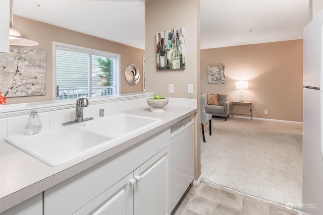 kitchen featuring light colored carpet, light countertops, white cabinets, white appliances, and a sink