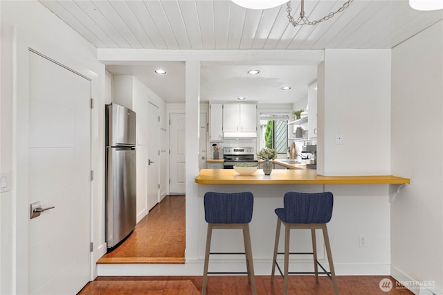 kitchen featuring a breakfast bar, tasteful backsplash, wooden ceiling, stainless steel appliances, and white cabinets