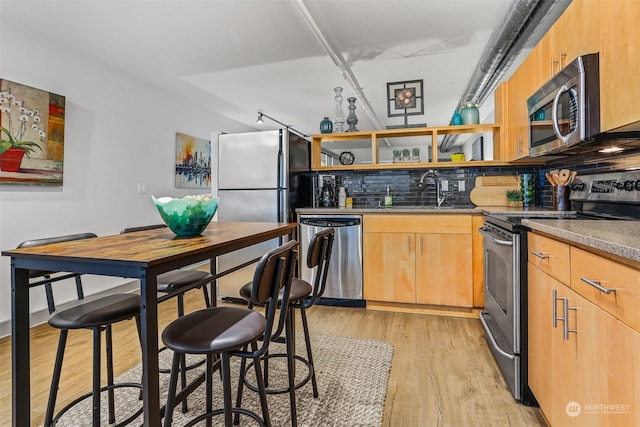 kitchen with stainless steel appliances, sink, tasteful backsplash, light hardwood / wood-style floors, and stone counters