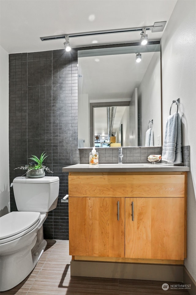 bathroom featuring toilet, tile walls, track lighting, tile patterned floors, and vanity