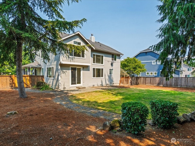 rear view of property featuring a yard, a chimney, and a fenced backyard