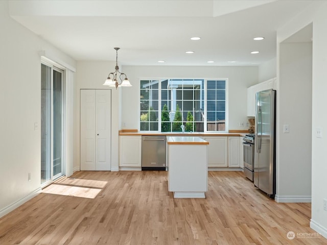 kitchen with decorative light fixtures, light wood finished floors, stainless steel appliances, light countertops, and white cabinets