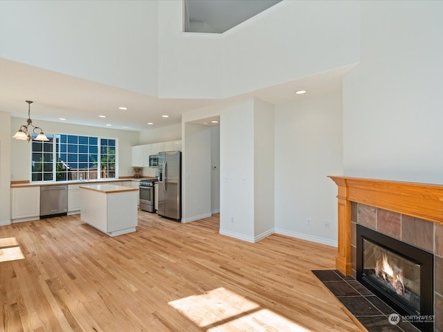 kitchen with white cabinetry, appliances with stainless steel finishes, a center island, a tiled fireplace, and decorative light fixtures