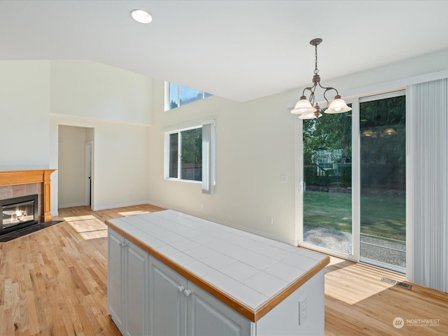 kitchen with tile counters, open floor plan, a fireplace, white cabinetry, and pendant lighting