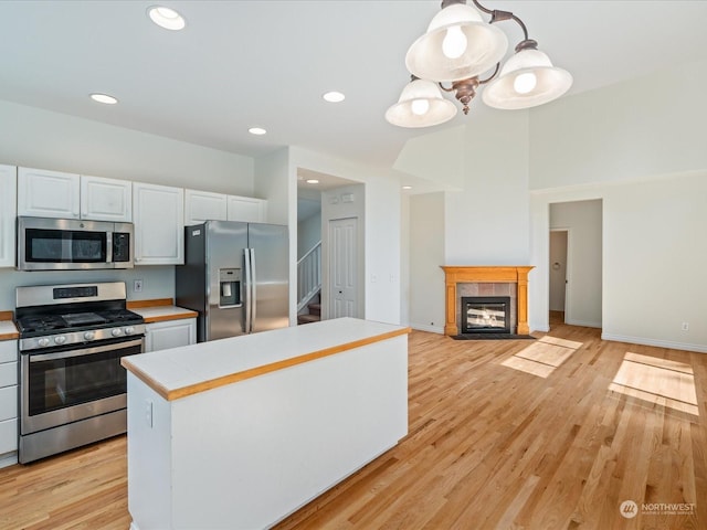 kitchen with white cabinets, open floor plan, decorative light fixtures, stainless steel appliances, and light wood-type flooring