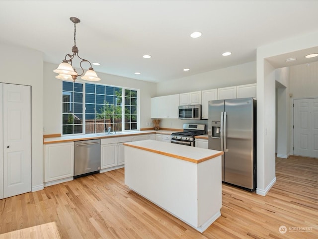 kitchen featuring stainless steel appliances, a kitchen island, white cabinetry, hanging light fixtures, and light countertops