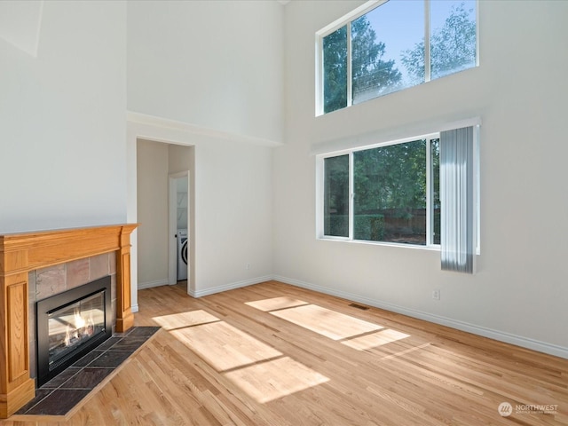 unfurnished living room featuring baseboards, washer / clothes dryer, a tiled fireplace, and wood finished floors