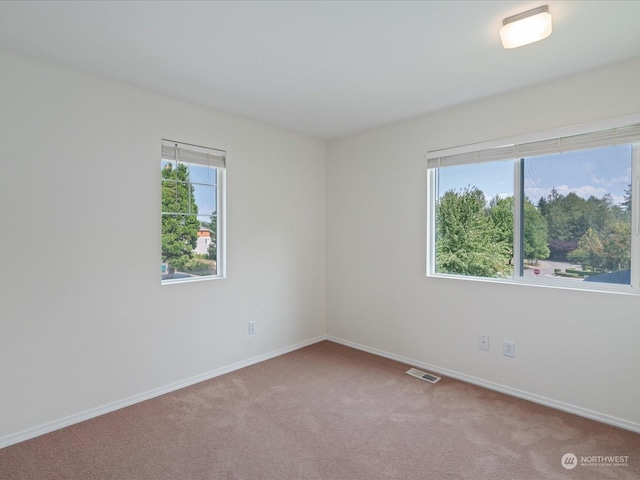 unfurnished room with carpet, visible vents, and baseboards