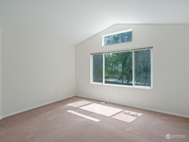 spare room featuring light colored carpet, vaulted ceiling, visible vents, and baseboards