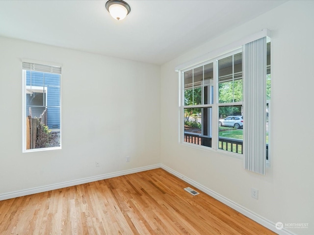 spare room featuring a healthy amount of sunlight, visible vents, light wood-style flooring, and baseboards