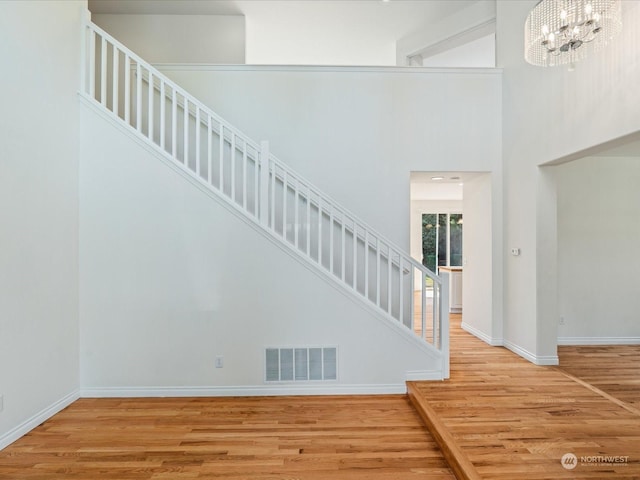 stairway with visible vents, a towering ceiling, wood finished floors, a chandelier, and baseboards