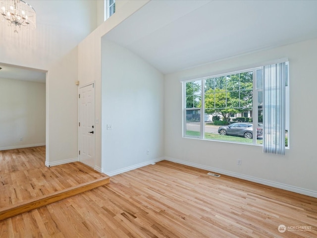 empty room with an inviting chandelier, light hardwood / wood-style floors, and a high ceiling