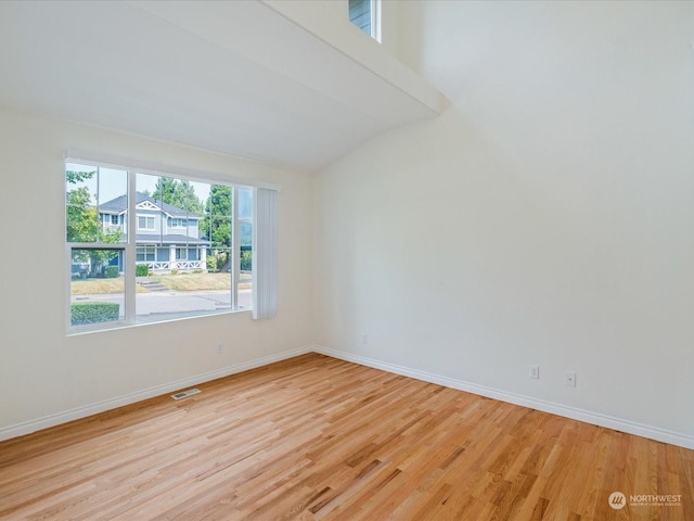 unfurnished room with light wood-style floors, lofted ceiling, visible vents, and baseboards