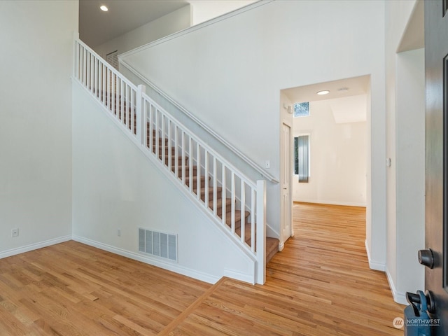 staircase featuring a towering ceiling, wood finished floors, visible vents, and baseboards