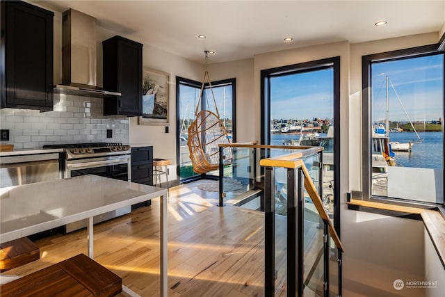 kitchen featuring a water view, wall chimney range hood, hanging light fixtures, and tasteful backsplash