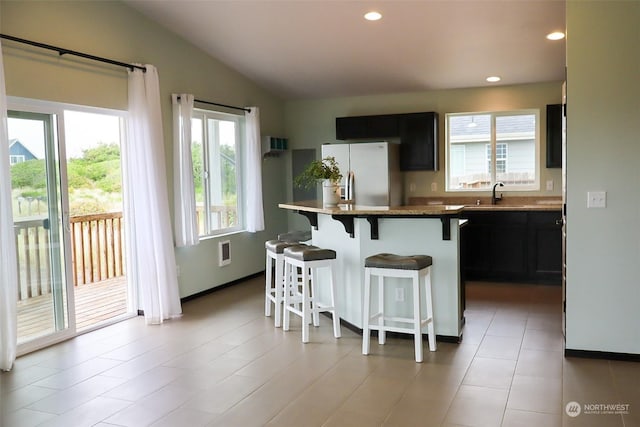 kitchen with lofted ceiling, sink, a breakfast bar area, a center island, and stainless steel refrigerator