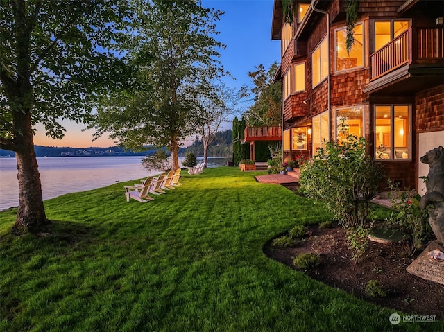 yard at dusk featuring a water view and a balcony