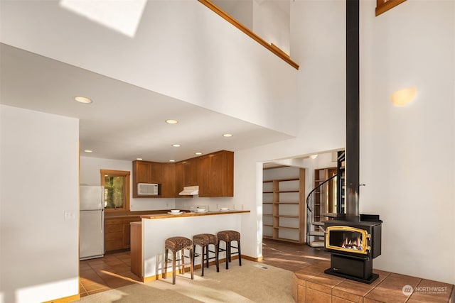 kitchen with tile patterned floors, white appliances, a wood stove, kitchen peninsula, and a kitchen bar