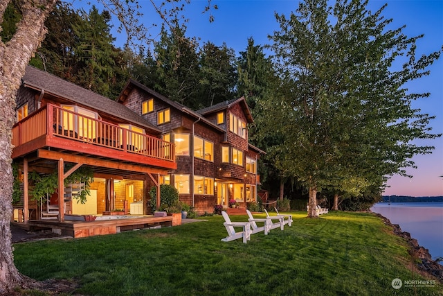 back house at dusk featuring a yard, a deck with water view, and a patio area