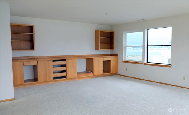 spare room with light carpet, built in study area, visible vents, and baseboards