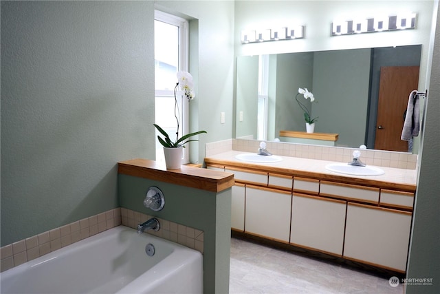 full bath featuring double vanity, a garden tub, a sink, and a textured wall