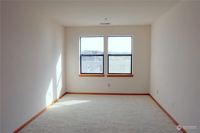 spare room with light carpet, visible vents, and baseboards