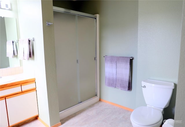 bathroom with toilet, a stall shower, vanity, and baseboards