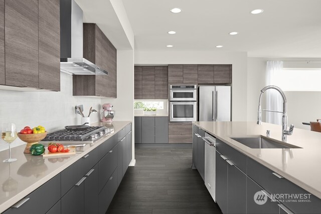 kitchen with dark hardwood / wood-style flooring, appliances with stainless steel finishes, sink, decorative backsplash, and wall chimney exhaust hood