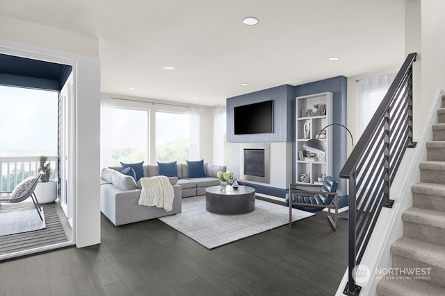 living area featuring dark wood-type flooring, stairway, a glass covered fireplace, and a healthy amount of sunlight