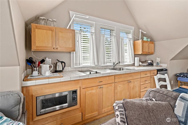 kitchen with tile counters, sink, light brown cabinets, and vaulted ceiling