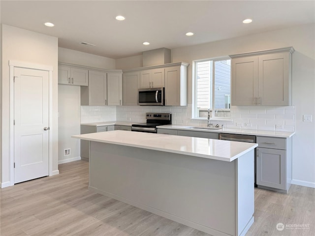 kitchen with a kitchen island, light wood-style flooring, gray cabinets, a sink, and appliances with stainless steel finishes