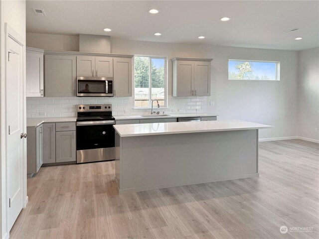 kitchen with appliances with stainless steel finishes, gray cabinets, sink, and a kitchen island