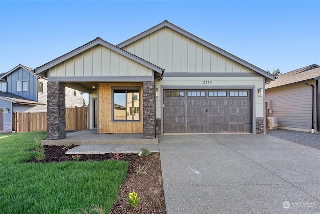 view of front of property featuring a front lawn, stone siding, fence, concrete driveway, and a garage