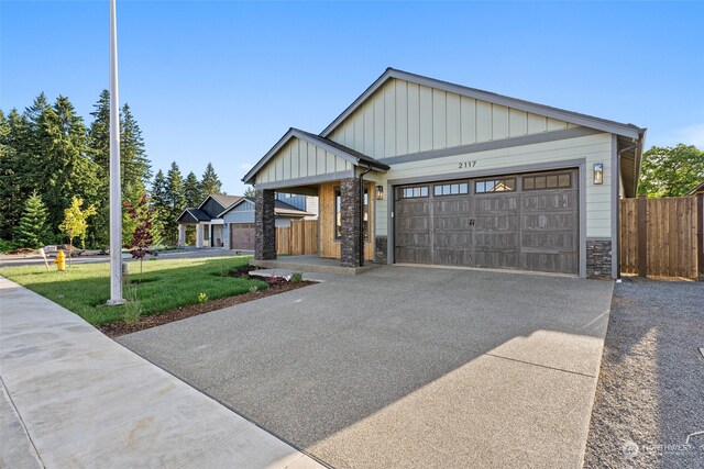 view of front of house featuring a front yard, driveway, an attached garage, stone siding, and board and batten siding