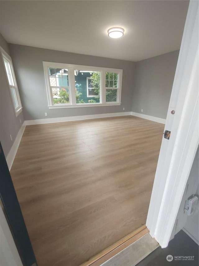 empty room with baseboards, light wood-type flooring, and a healthy amount of sunlight