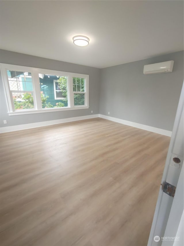 empty room with light wood-style floors, an AC wall unit, and baseboards