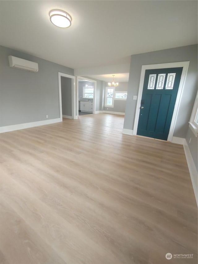 entryway with a wall unit AC, an inviting chandelier, light wood-style flooring, and baseboards