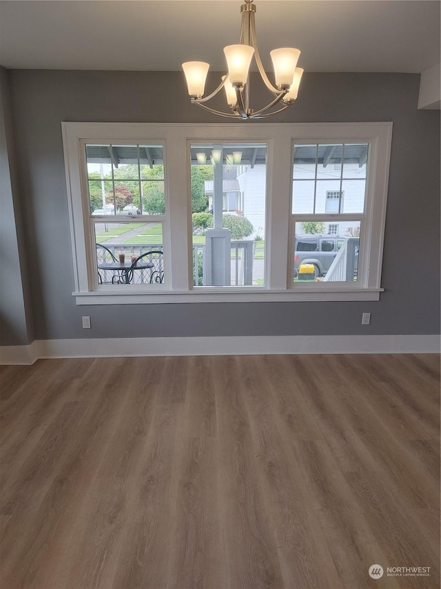 unfurnished dining area featuring an inviting chandelier, baseboards, and wood finished floors