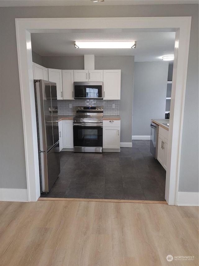 kitchen featuring white cabinets, decorative backsplash, appliances with stainless steel finishes, dark wood-type flooring, and light countertops