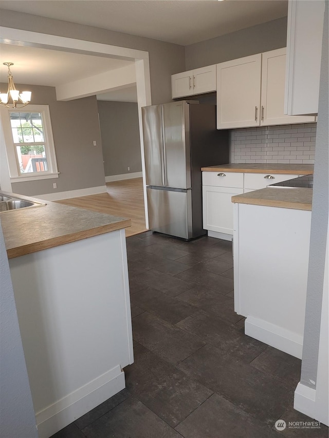 kitchen featuring a notable chandelier, a sink, white cabinets, freestanding refrigerator, and tasteful backsplash