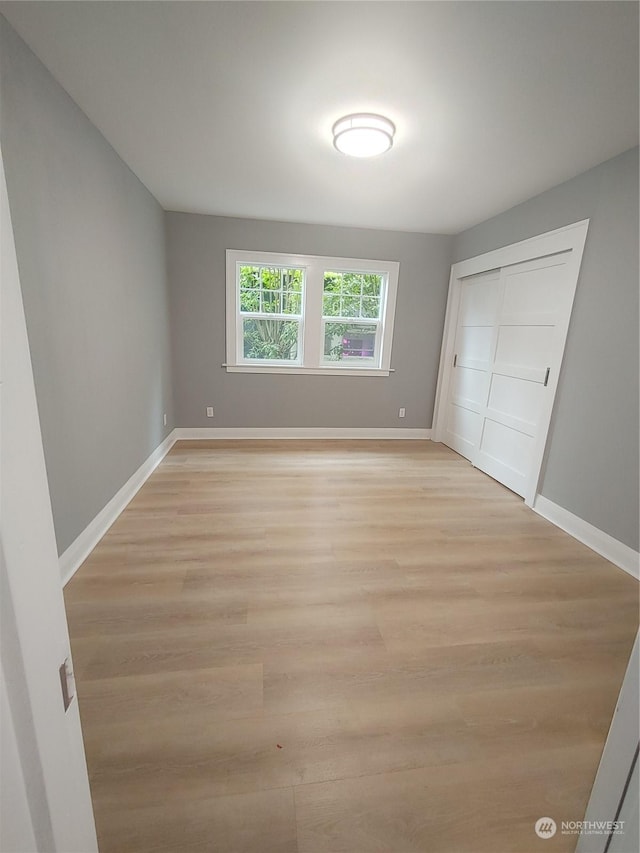 unfurnished bedroom with light wood-style floors, a closet, and baseboards