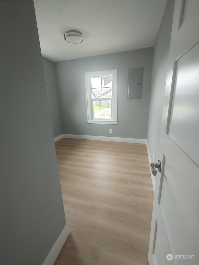 empty room with light wood-style floors, electric panel, and baseboards