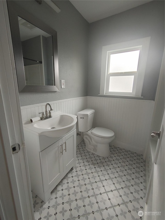 bathroom with toilet, wainscoting, vanity, and tile patterned floors