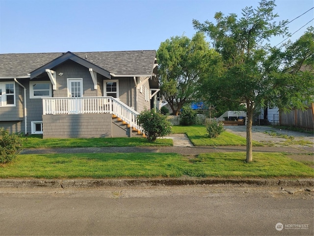 view of front of property with covered porch, roof with shingles, stairway, and a front yard