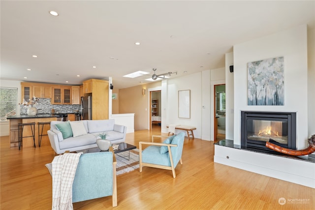 living room with a skylight, ceiling fan, and light hardwood / wood-style floors