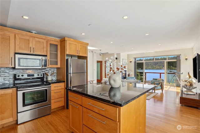 kitchen with backsplash, stainless steel appliances, dark stone countertops, light hardwood / wood-style floors, and a kitchen island