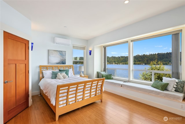 bedroom with an AC wall unit, light hardwood / wood-style flooring, and a water view