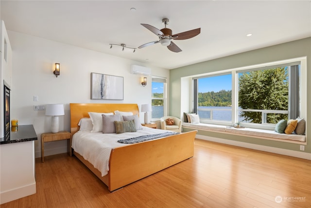 bedroom featuring light hardwood / wood-style floors, an AC wall unit, ceiling fan, and a water view