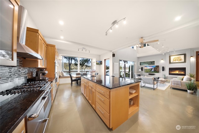 kitchen featuring ceiling fan, wall chimney range hood, dark stone countertops, oven, and decorative backsplash